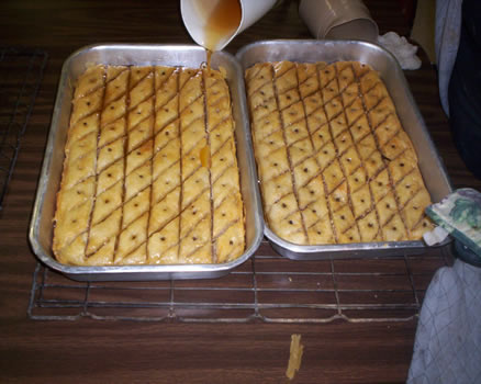 Pouring a honey-lemon-spice syrup over hot baklava